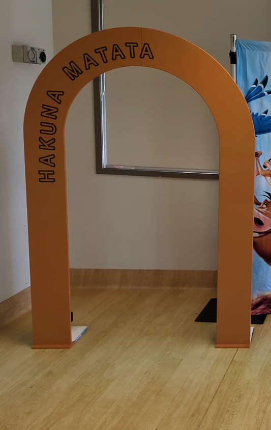 Orange arch with 'Hakuna Matata' text next to a Lion King poster on a wall. Prop hire, Prop hiring, Prop hire, event stylists Brisbane, brisbane event styling, brisbane event styling, event stylist Brisbane, Brisbane Wedding, Gold Coast Wedding, Floral Styling, Lush & Lavish Events, Brisbane Corporate Styling, Gold Coast Corporate Styling, Brisbane Brand Activation, Gold Coast Tablescapes, Brisbane Candle Hire
