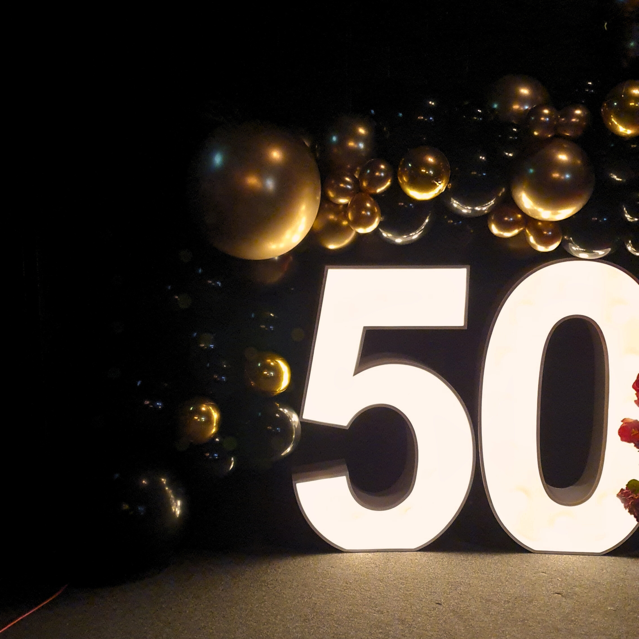 Close-up of white '50' surrounded by gold and black balloons against a dark background. Prop hire, Prop hiring, Prop hire, event stylists Brisbane, brisbane event styling, brisbane event styling, event stylist Brisbane, Brisbane Wedding, Gold Coast Wedding, Floral Styling, Lush & Lavish Events, Brisbane Tablescape, Gold Coast Tablescapes, Brisbane Candle Hire