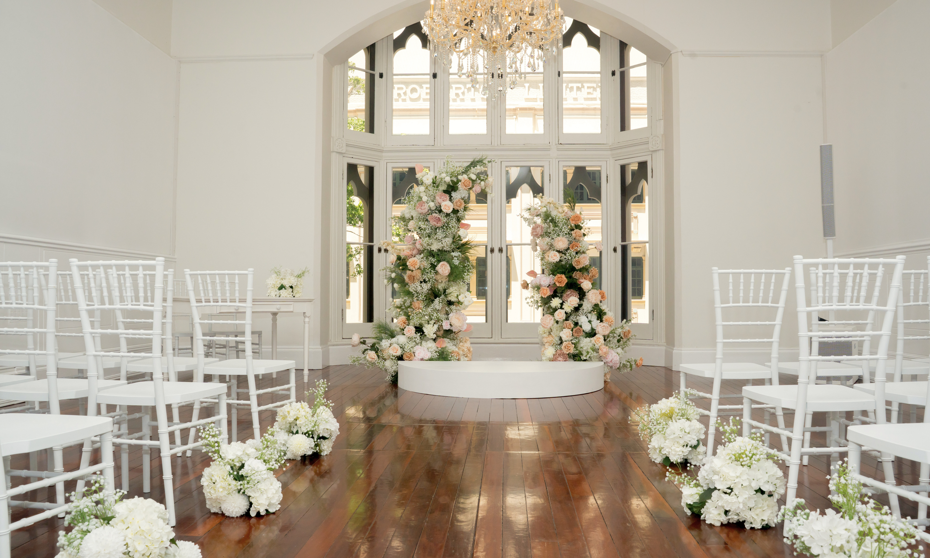 Decorated wedding ceremony space with floral arrangements and white chairs. the little laneway wedding styling, the little laneway brisbane wedding venue styling, wedme brisbane wedding vendor, wedme co brisbane wedding trail, brisbane wedding styling, brisbane wedding stylist, luxury wedding styling brisbane, wedding ceremony styling brisbane, wedding reception styling brisbane, wedding altar styling brisbane, bridal table styling ideas, guest table wedding styling, wedding aisle styling ideas.