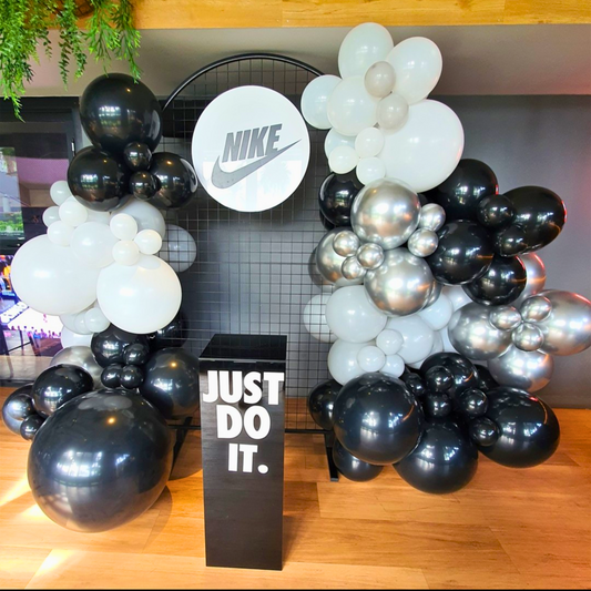 Nike display with black, white, and metallic balloons around a circular logo sign and 'JUST DO IT.' slogan on a black pedestal. Prop hire, Prop hiring, Prop hire, event stylists Brisbane, brisbane event styling, brisbane event styling, event stylist Brisbane, Brisbane Wedding, Gold Coast Wedding, Floral Styling, Lush & Lavish Events, Brisbane Corporate Styling, Gold Coast Corporate Styling, Brisbane Brand Activation