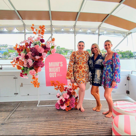 Four people on a boat deck with vibrant floral arrangements and a pink 'MUM’S NIGHT OUT' sign. Prop hire, Prop hiring, Prop hire, event stylists Brisbane, brisbane event styling, brisbane event styling, event stylist Brisbane, Brisbane Wedding, Gold Coast Wedding, Floral Styling, Lush & Lavish Events, Brisbane Tablescape, Gold Coast Tablescapes, Brisbane Candle Hire