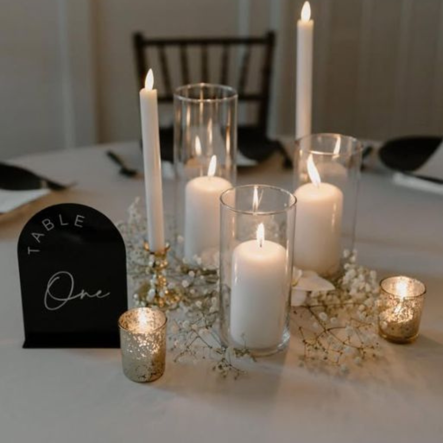 Candlelit table setting with 'Table One' sign on a white tablecloth.