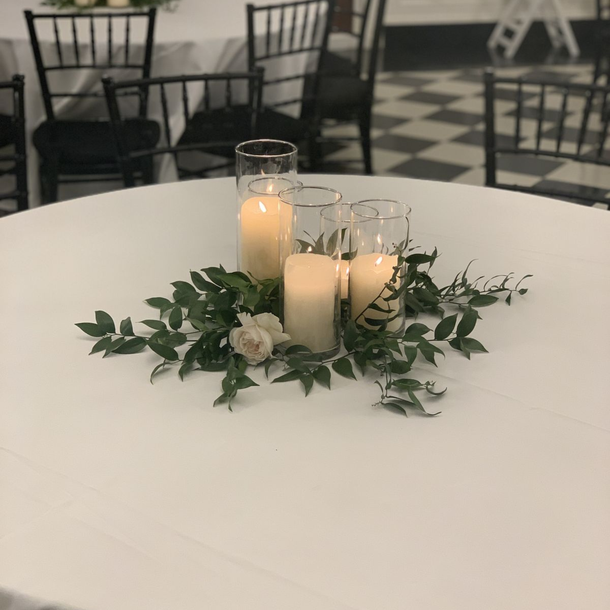 Decorative table centerpiece with candles and greenery on a white table.