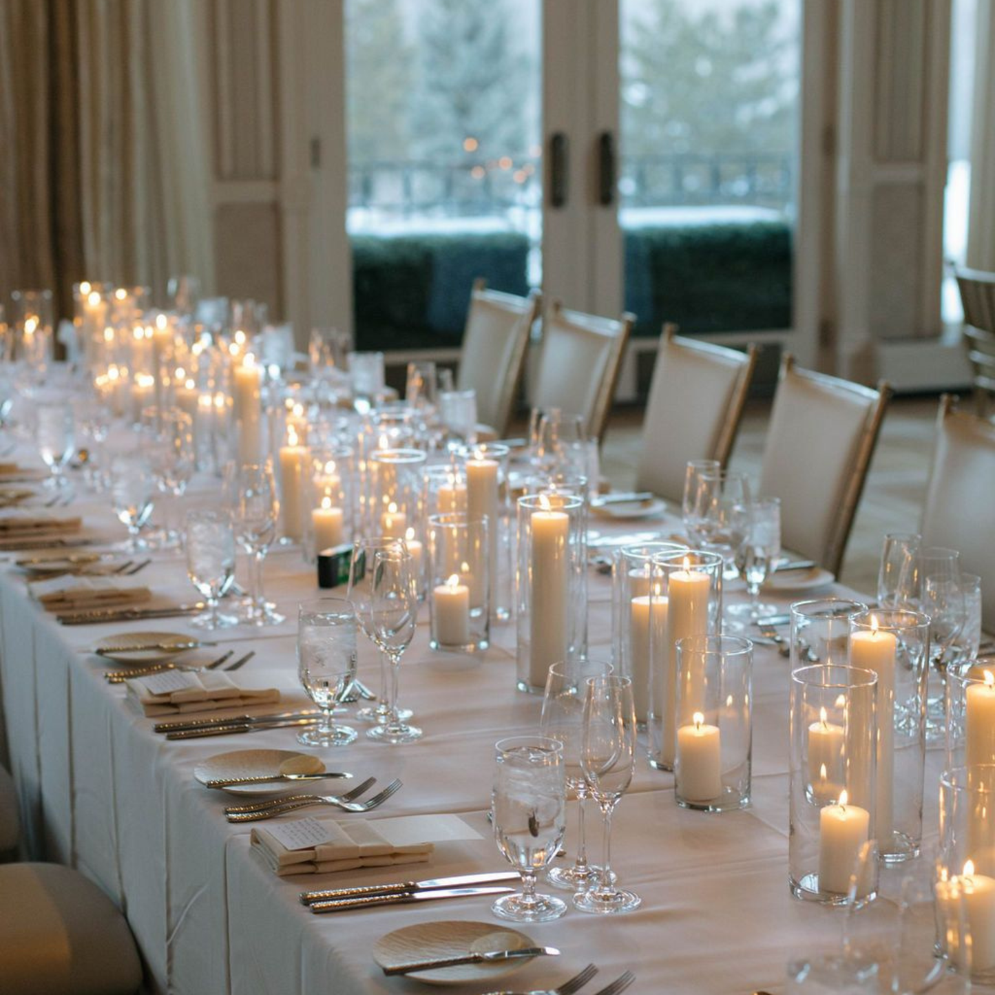 Elegant long table set for a formal event with candles, glasses, and cutlery.
