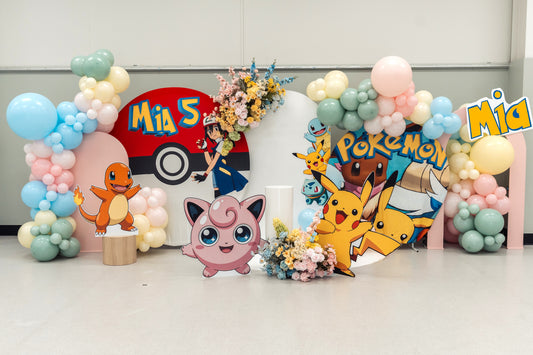 Full view of a Pokémon 5th birthday display with a red Poké Ball panel, pastel balloon garlands, character cut-outs and floral arrangements.