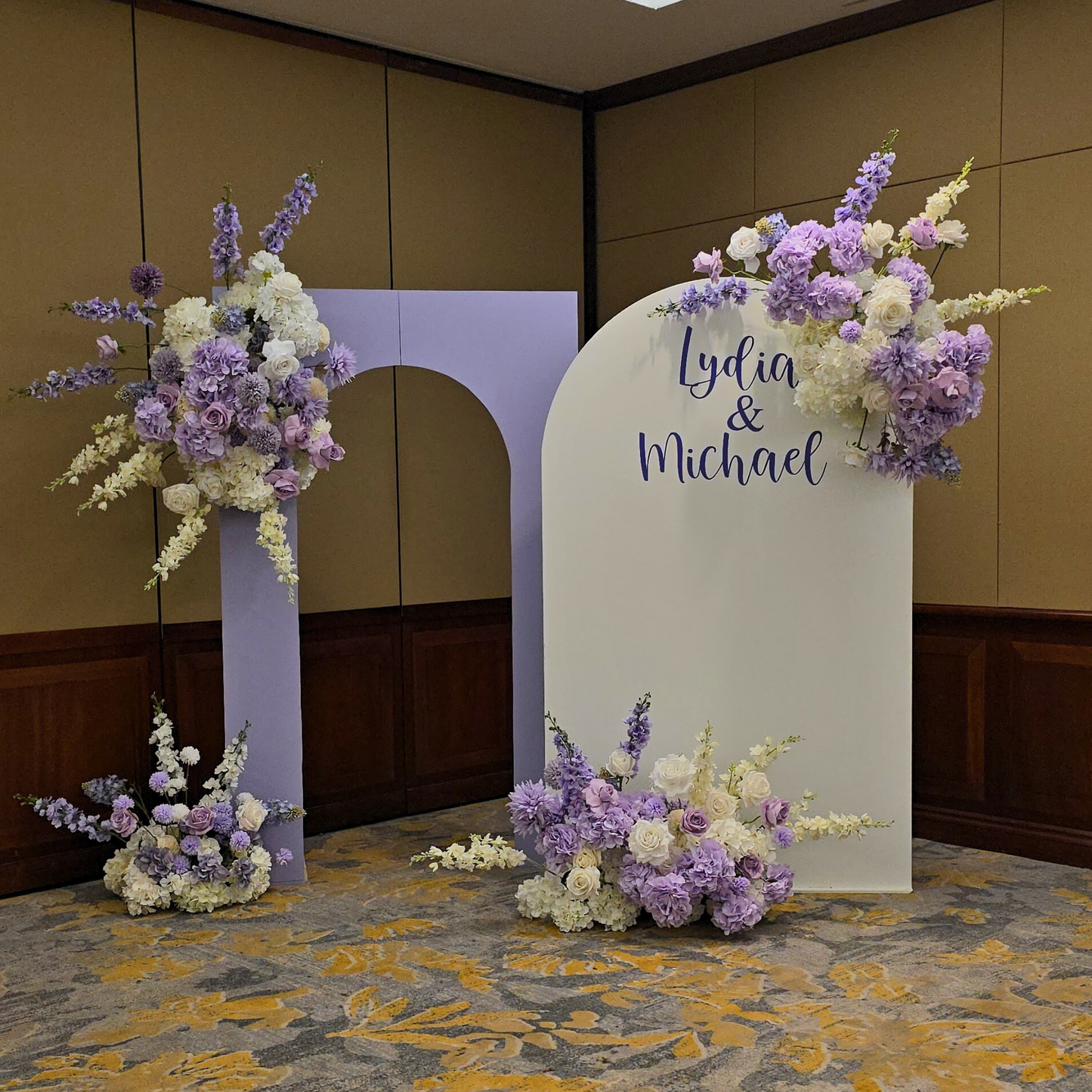Floral backdrop in purple and white with "Lydia & Michael" on the largest arch. Prop hire, Prop hiring, Prop hire, event stylists Brisbane, brisbane event styling, brisbane event styling, event stylist Brisbane, Brisbane Wedding, Gold Coast Wedding, Floral Styling, Lush & Lavish Events, Brisbane Corporate Styling, Gold Coast Corporate Styling, Brisbane Brand Activation, Gold Coast Tablescapes, Brisbane Candle Hire