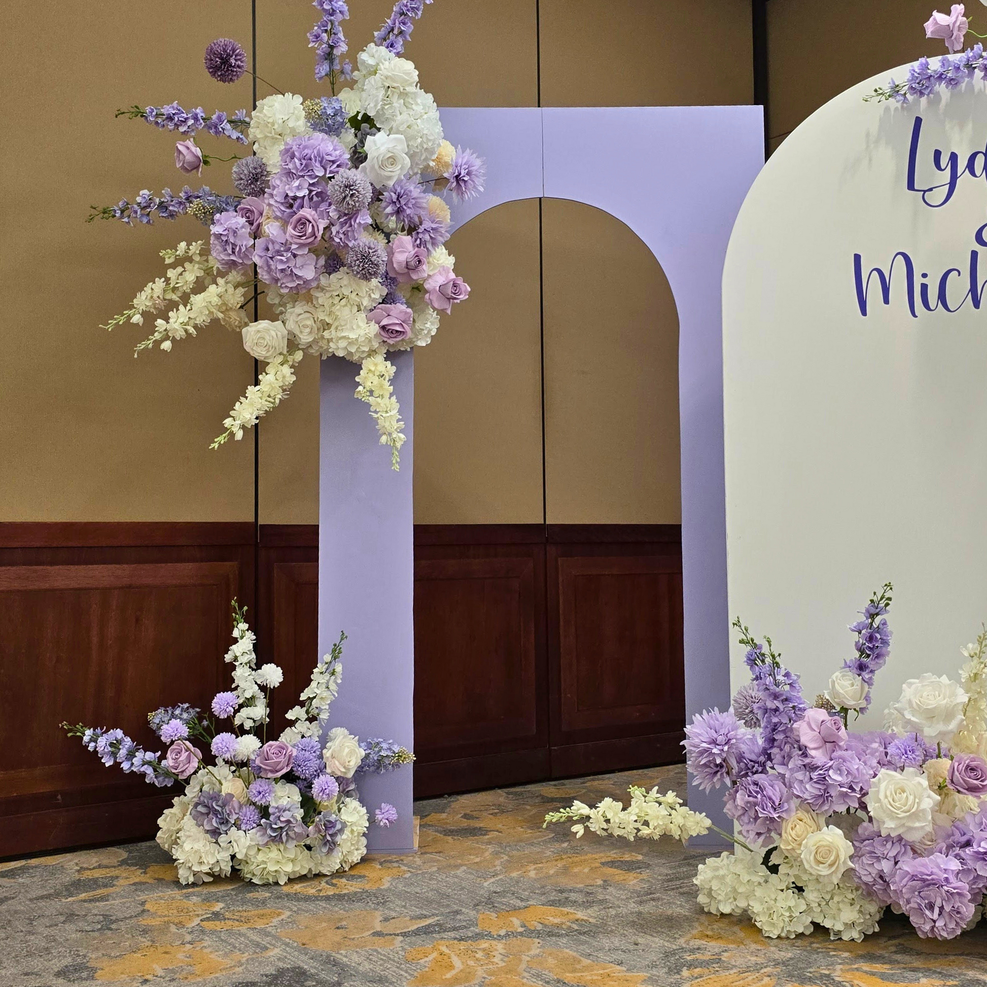 Floral backdrop in purple and white with "Lydia & Michael" on the largest arch. Prop hire, Prop hiring, Prop hire, event stylists Brisbane, brisbane event styling, brisbane event styling, event stylist Brisbane, Brisbane Wedding, Gold Coast Wedding, Floral Styling, Lush & Lavish Events, Brisbane Corporate Styling, Gold Coast Corporate Styling, Brisbane Brand Activation, Gold Coast Tablescapes, Brisbane Candle Hire