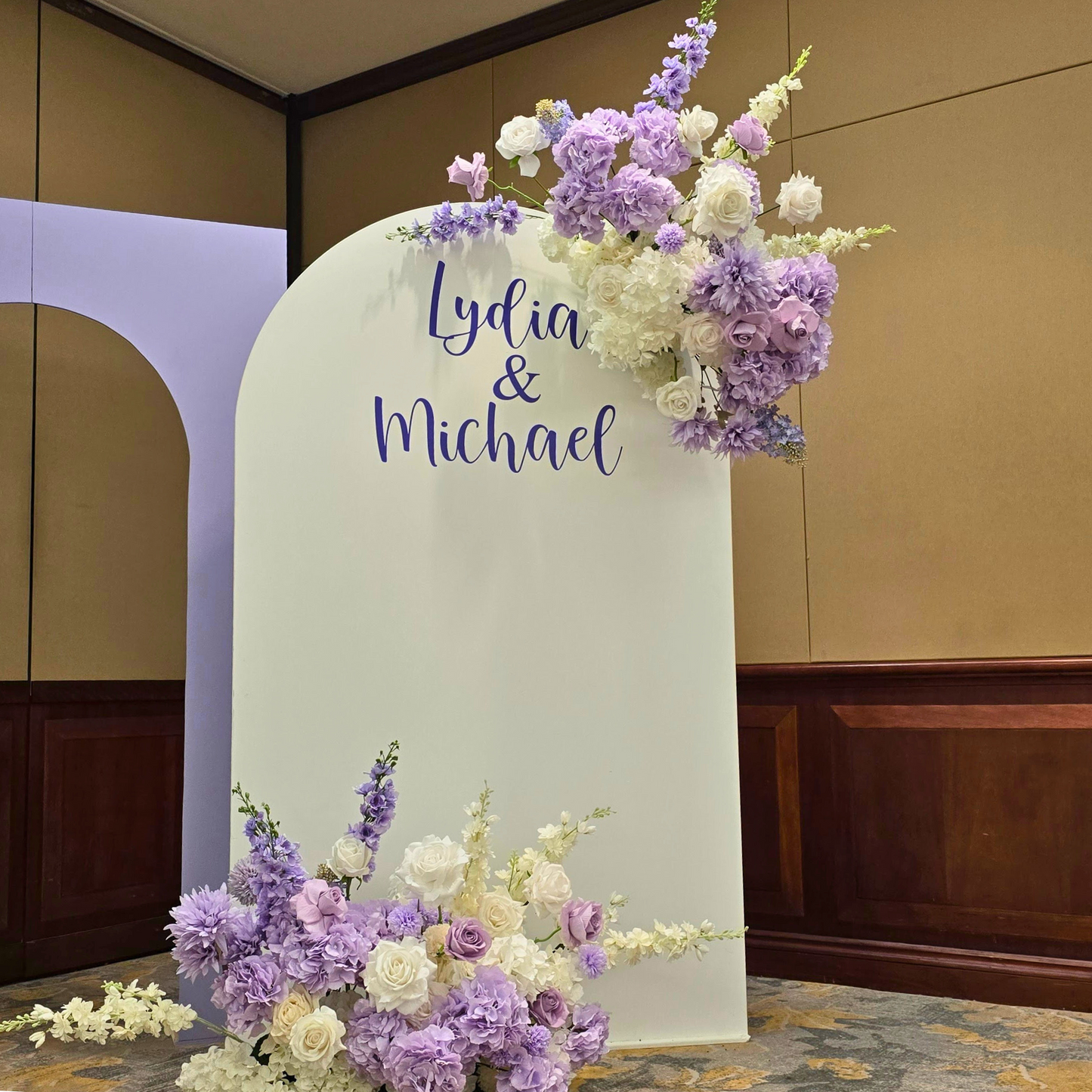 Floral backdrop in purple and white with "Lydia & Michael" on the largest arch. Prop hire, Prop hiring, Prop hire, event stylists Brisbane, brisbane event styling, brisbane event styling, event stylist Brisbane, Brisbane Wedding, Gold Coast Wedding, Floral Styling, Lush & Lavish Events, Brisbane Corporate Styling, Gold Coast Corporate Styling, Brisbane Brand Activation, Gold Coast Tablescapes, Brisbane Candle Hire