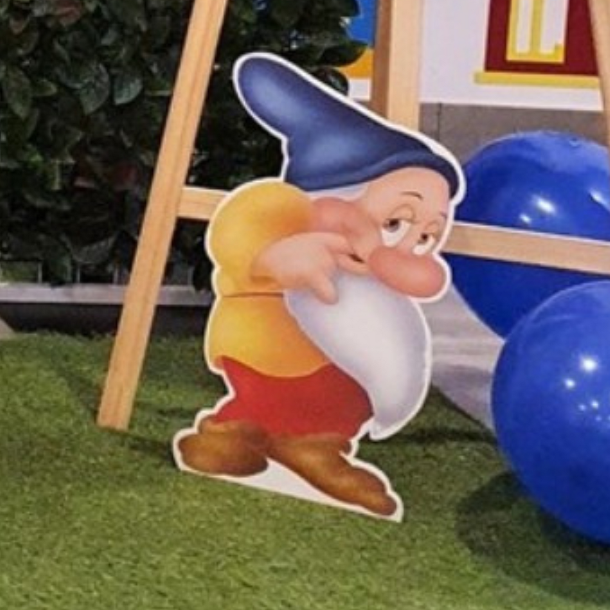 Cutout of a dwarf character from Snow White, positioned in front of colorful balloons with a blurred background, ideal for themed parties or events. Prop hire, Prop hiring, Prop hire, event stylists Brisbane, brisbane event styling, brisbane event styling, event stylist Brisbane, Brisbane Wedding, Gold Coast Wedding, Floral Styling, Lush & Lavish Events, Brisbane Tablescape, Gold Coast Tablescapes, Brisbane Candle Hire