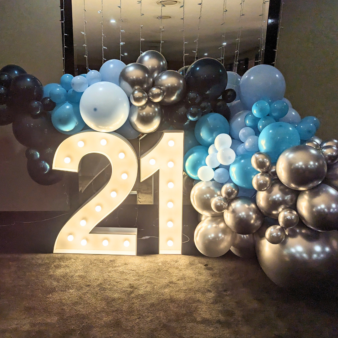 A 21st birthday backdrop featuring a large number 21, surrounded by silver and teal balloons, with a luxury organic balloon garland in the background. Styled by Lush and Lavish Events a Brisbane and Gold Coast based event planning, event styling, Event MC services and on-the-day coordination business.