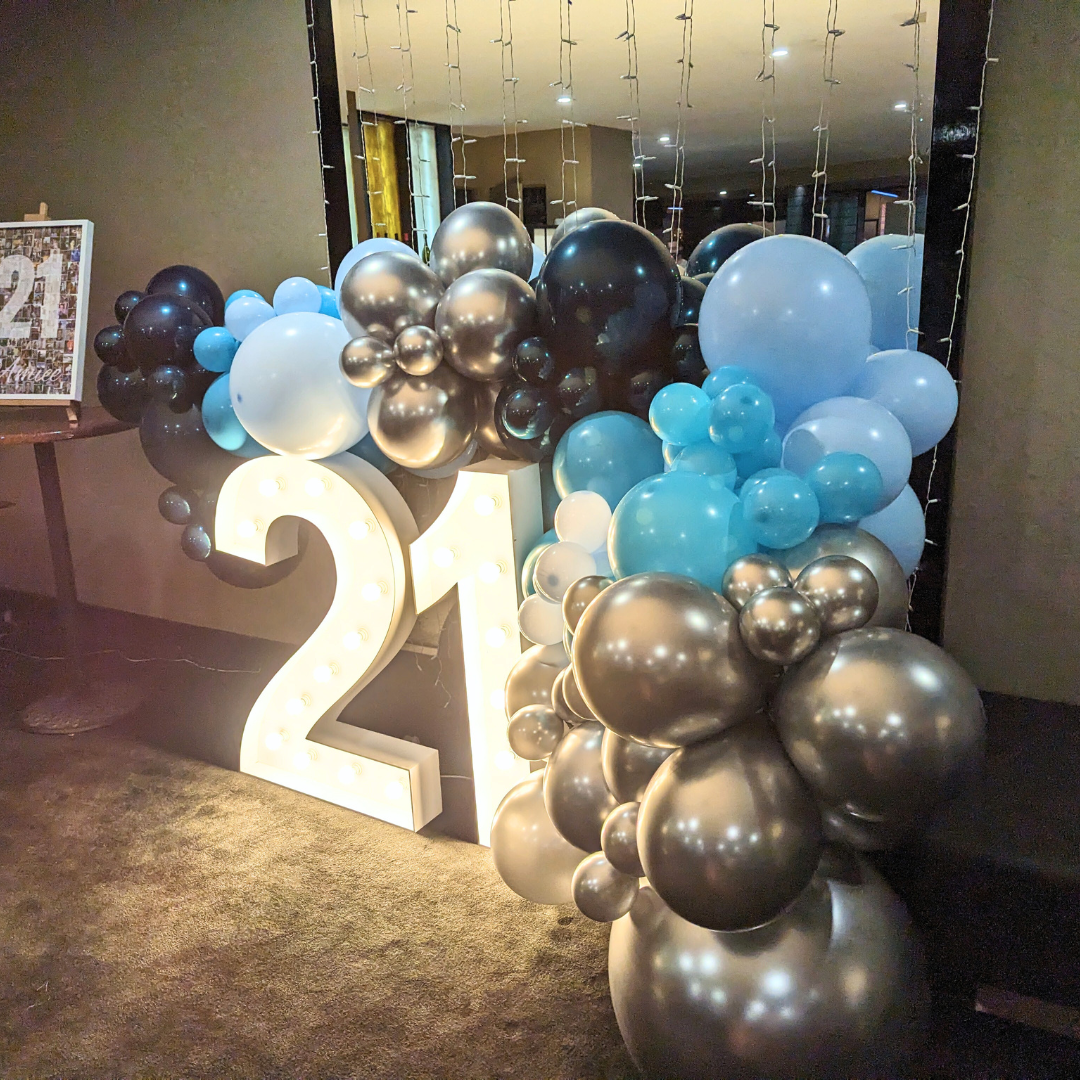 A 21st birthday backdrop featuring a large number 21, surrounded by silver and teal balloons, with a luxury organic balloon garland in the background. Styled by Lush and Lavish Events a Brisbane and Gold Coast based event planning, event styling, Event MC services and on-the-day coordination business.