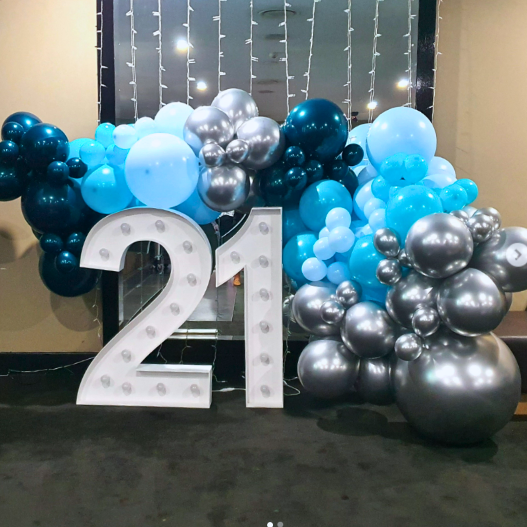 A 21st birthday backdrop featuring a large number 21, surrounded by silver and teal balloons, with a luxury organic balloon garland in the background. Styled by Lush and Lavish Events a Brisbane and Gold Coast based event planning, event styling, Event MC services and on-the-day coordination business.