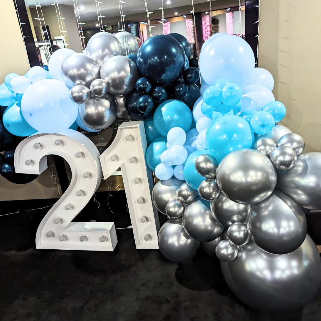 A 21st birthday backdrop featuring a large number 21, surrounded by silver and teal balloons, with a luxury organic balloon garland in the background. Styled by Lush and Lavish Events a Brisbane and Gold Coast based event planning, event styling, Event MC services and on-the-day coordination business.