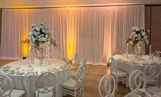 Full white pleated drape backdrop spanning the reception wall with a warm glow across the fabric.