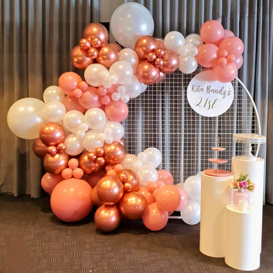 A balloon arch with white, pink, and rose gold balloons frames a dessert table with a two-tiered cake and signage for Kita Bandz's 21st birthday. Prop hire, Prop hiring, Prop hire, event stylists Brisbane, brisbane event styling, brisbane event styling, event stylist Brisbane, Brisbane Wedding, Gold Coast Wedding, Floral Styling, Lush & Lavish Events, Brisbane Tablescape, Gold Coast Tablescapes, Brisbane Candle Hire