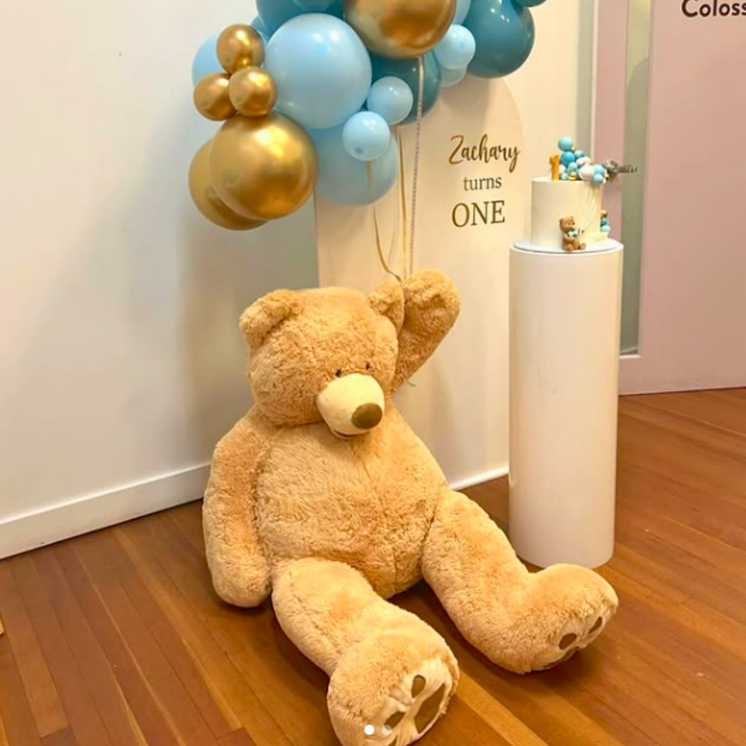 Large teddy bear on a wooden floor with balloons and a cake in the background. Prop hire, Prop hiring, Prop hire, event stylists Brisbane, brisbane event styling, brisbane event styling, event stylist Brisbane, Brisbane Wedding, Gold Coast Wedding, Floral Styling, Lush & Lavish Events, Brisbane Corporate Styling, Gold Coast Corporate Styling, Brisbane Brand Activation, Gold Coast Tablescapes, Brisbane Candle Hire